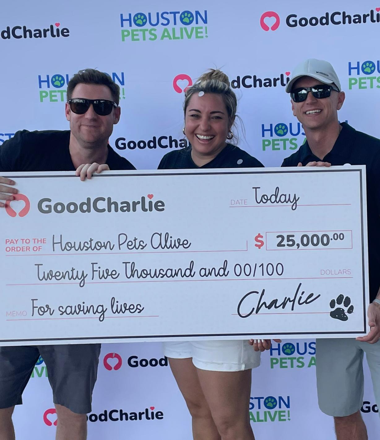 Daryl and Ken, cofounders of GoodCharlie, together with a woman, hold a giant dummy cheque of $25,000 issued to Houston Pets Alive organisation.