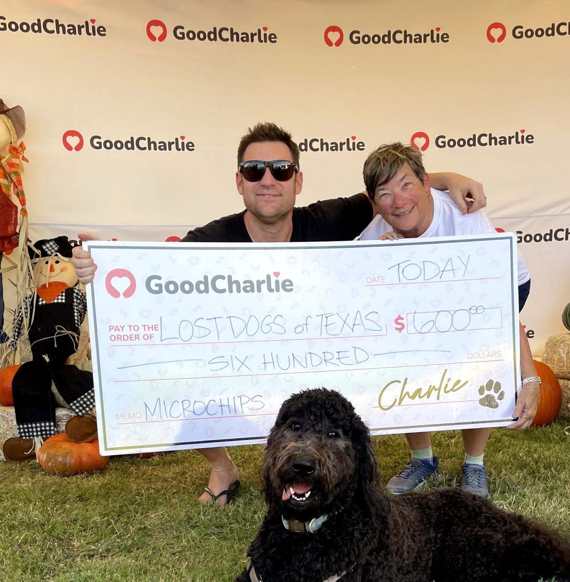 Daryl, cofounder of GoodCharlie, presenting a $600 cheque to Marilyn Litt, director of Lost Dogs of Texas. Charlie is sitting on the grass in front of them.